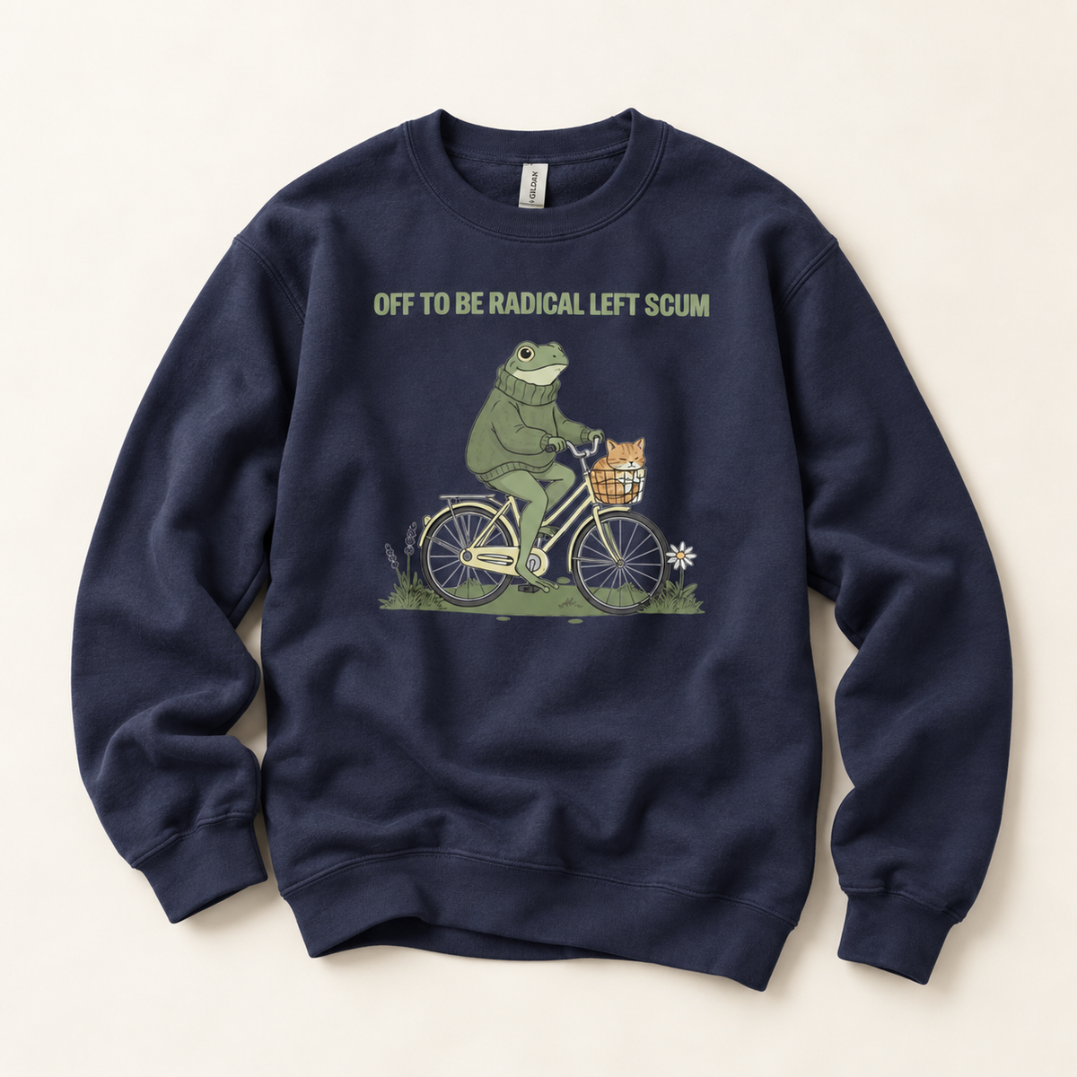 A navy blue crewneck sweatshirt featuring a graphic of a green frog riding a bicycle with a small orange cat in the basket, with the text 'OFF TO BE RADICAL LEFT SCUM' printed above. The sweatshirt is laid flat on a light beige background.