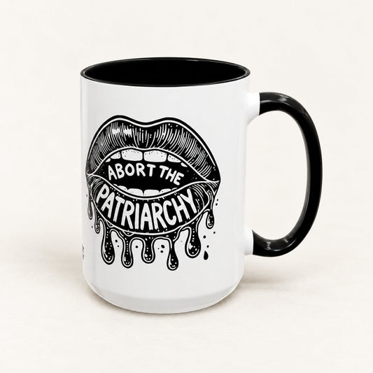 Abort the Patriarchy 15 oz tall white coffee mug with black handle on a warm off-white background