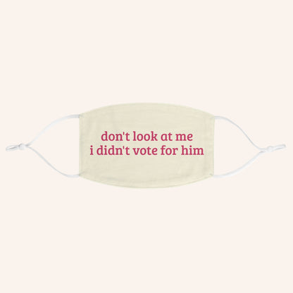 A cream-colored fabric face mask with white ear loops and pink printed text that reads 'don't look at me i didn't vote for him'.