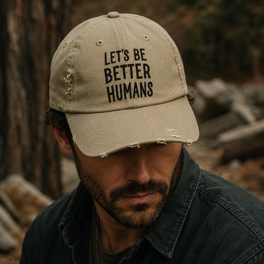Man wearing a cap with 'Let's Be Better Humans' text in a forest setting