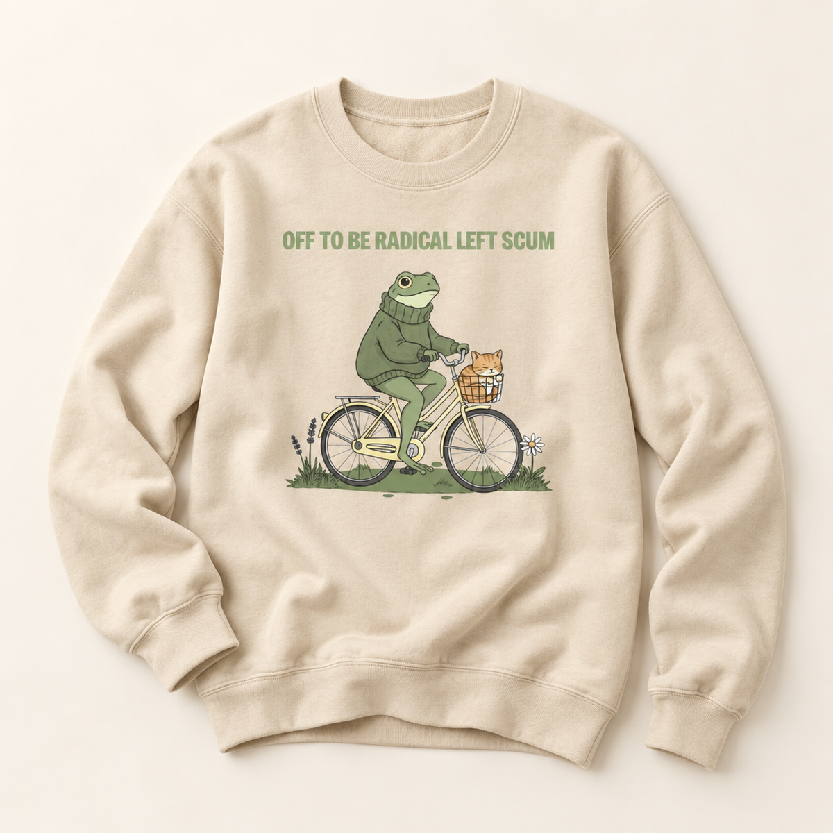 A beige crewneck sweatshirt featuring a graphic of a green frog riding a white bicycle with a basket, accompanied by the text 'OFF TO BE RADICAL LEFT SCUM'.