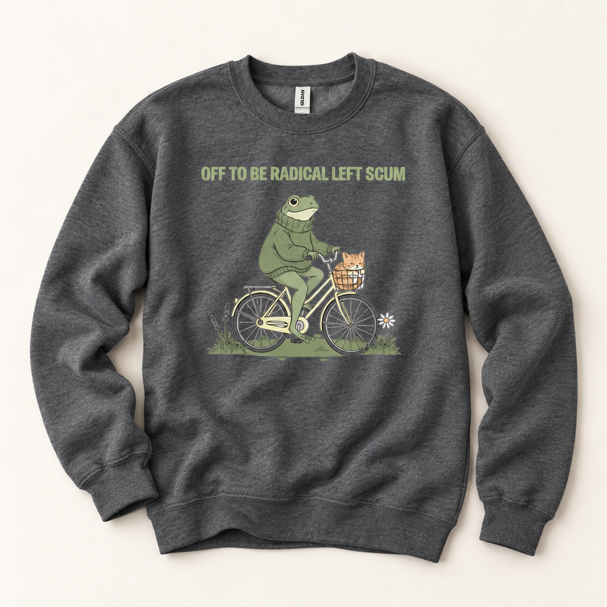 A dark heather gray crewneck sweatshirt featuring a graphic of a green frog riding a bicycle with a small orange cat in the basket. Above the graphic, the text reads 'OFF TO BE RADICAL LEFT SCUM' in a muted olive green font.