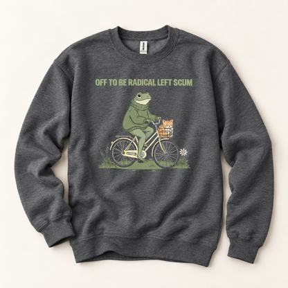 A dark heather gray crewneck sweatshirt featuring a graphic of a green frog riding a bicycle with a small orange cat in the basket. Above the graphic, the text reads 'OFF TO BE RADICAL LEFT SCUM' in a muted olive green font.
