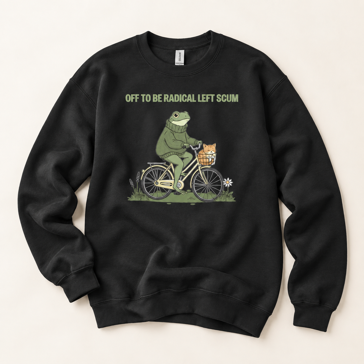 A black crewneck sweatshirt featuring a graphic of a green frog riding a bicycle with a basket, accompanied by the text 'OFF TO BE RADICAL LEFT SCUM' in olive green. The sweatshirt is laid flat on a light beige background.