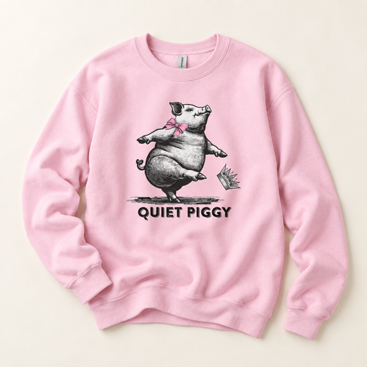 A light pink crewneck sweatshirt featuring a graphic of a cartoon pig wearing a pink bow and the text 'QUIET PIGGY' printed below, displayed flat against a light beige background.
