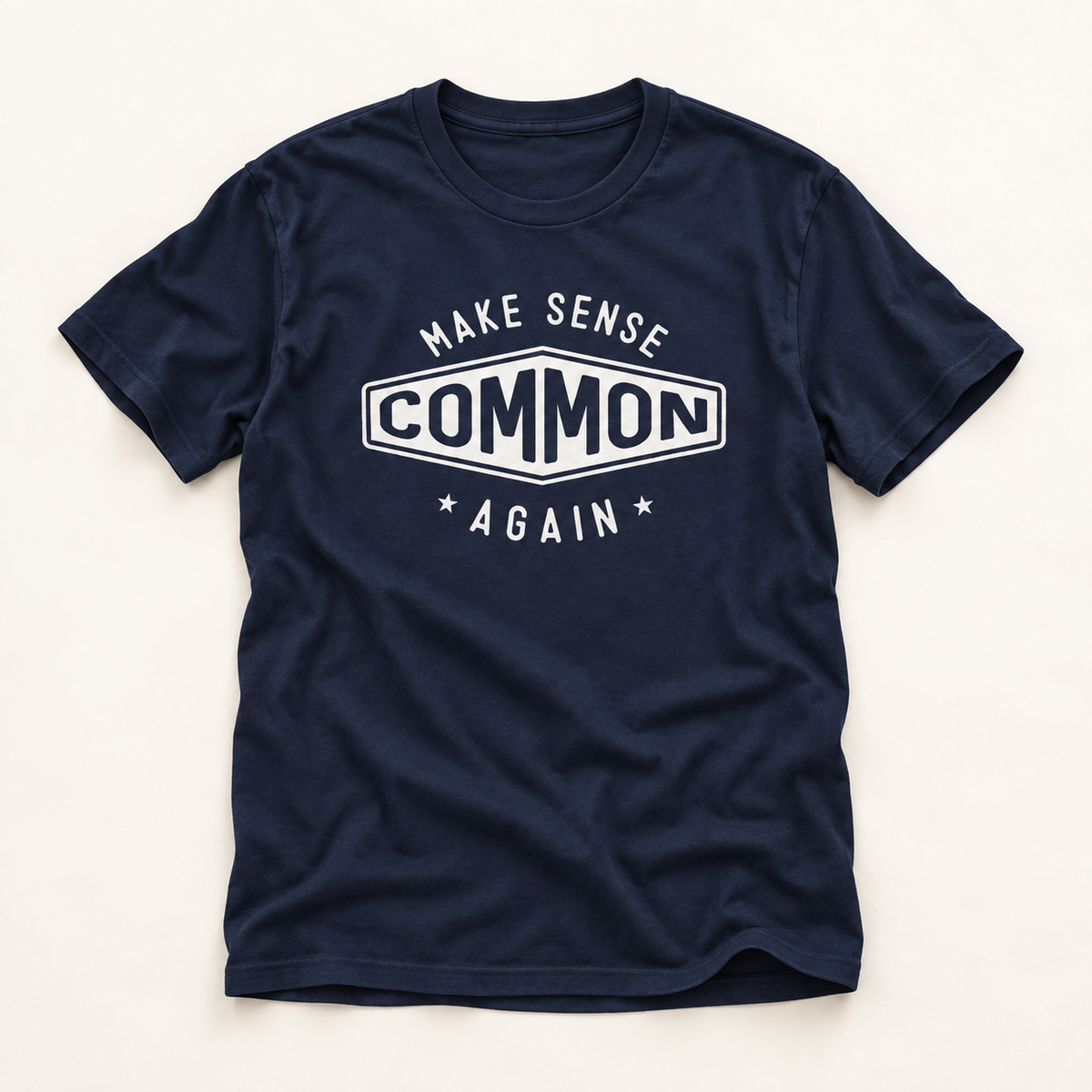 A navy blue short-sleeve t-shirt with a white graphic print on the chest that reads 'MAKE SENSE COMMON AGAIN' with stars, laid flat on a light beige background.