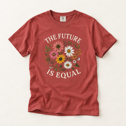 A rust red short-sleeve t-shirt with a graphic print that reads 'THE FUTURE IS EQUAL' in white arched text surrounding a colorful floral design. The shirt is laid flat on a light beige background.